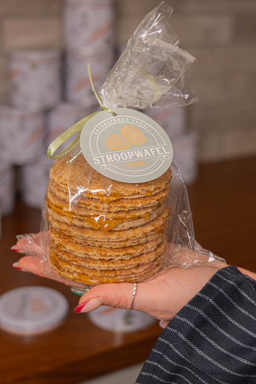 Stack of stroopwafels in clear plastic wrap with a visible brand label, held by a person.