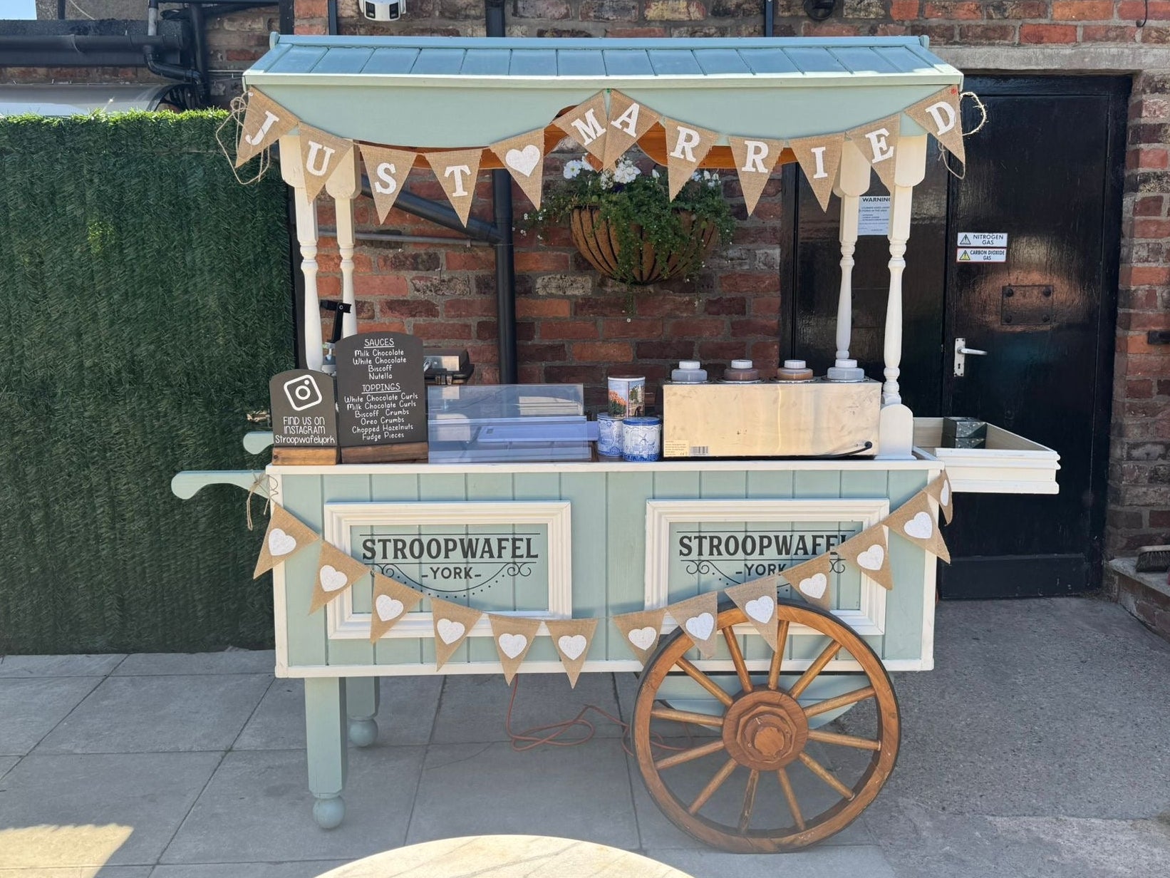 Vintage-style ice cream cart with 'HAPPILY MARRIED' banner in front of a brick building.